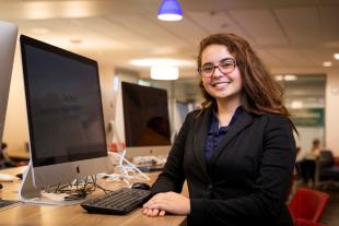 A student sits in front of a computer and smiles on Cal Poly's campus during the Volunteer Income Tax Assistance program.