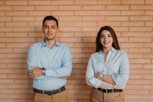 Amirsalar Pardakhti and Nooshin Shafiee stand in blue shirts in front of a brick wall.