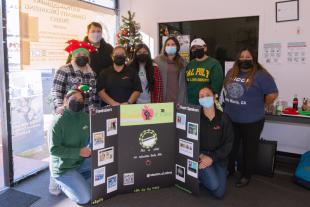 A group of masked students representing the Educators of Color club pose with a posterboard during a holiday book and gift drive.