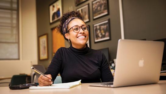 A Cal Poly student smiles broadly during her internship while sitting at her computer