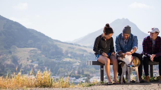 Three students sitting on a bench on Madonna Mountain with a dog