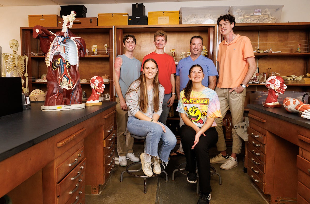 A group of students and a professor, surrounded by anatomical models, pose for a group photo.