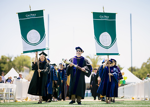 The commencement stage officials march in carrying college banners and the ceremonial mace at the 2023 commencement ceremony held at Spanos Stadium