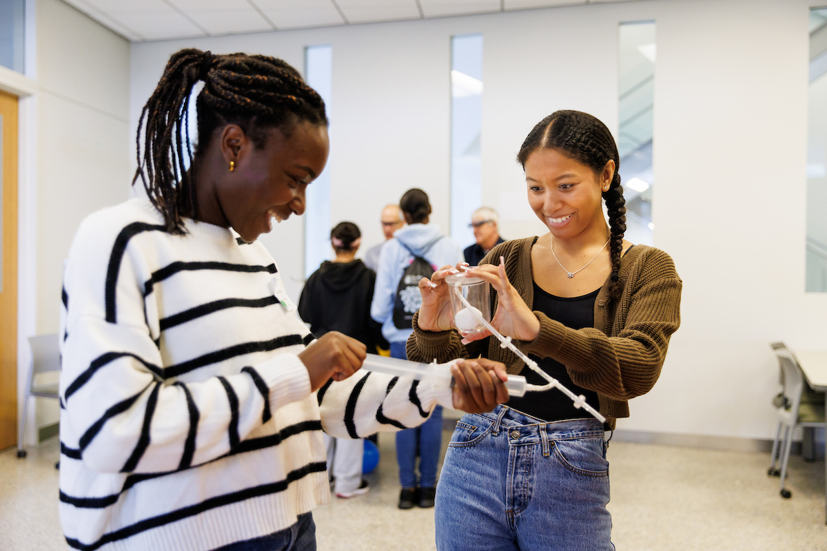 Two students engage with an object containing tubes during a Baily College of Science and Math demonstration.