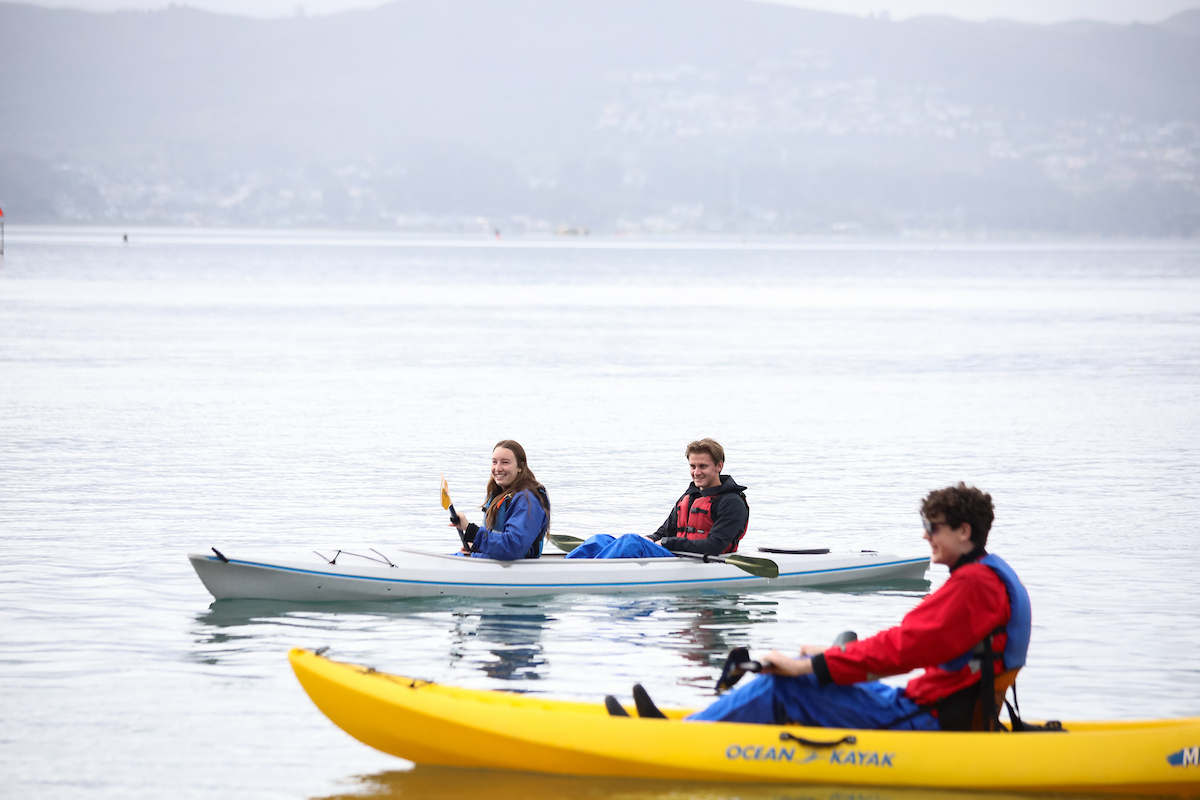 Three students paddle kayaks in Morro Bay. 