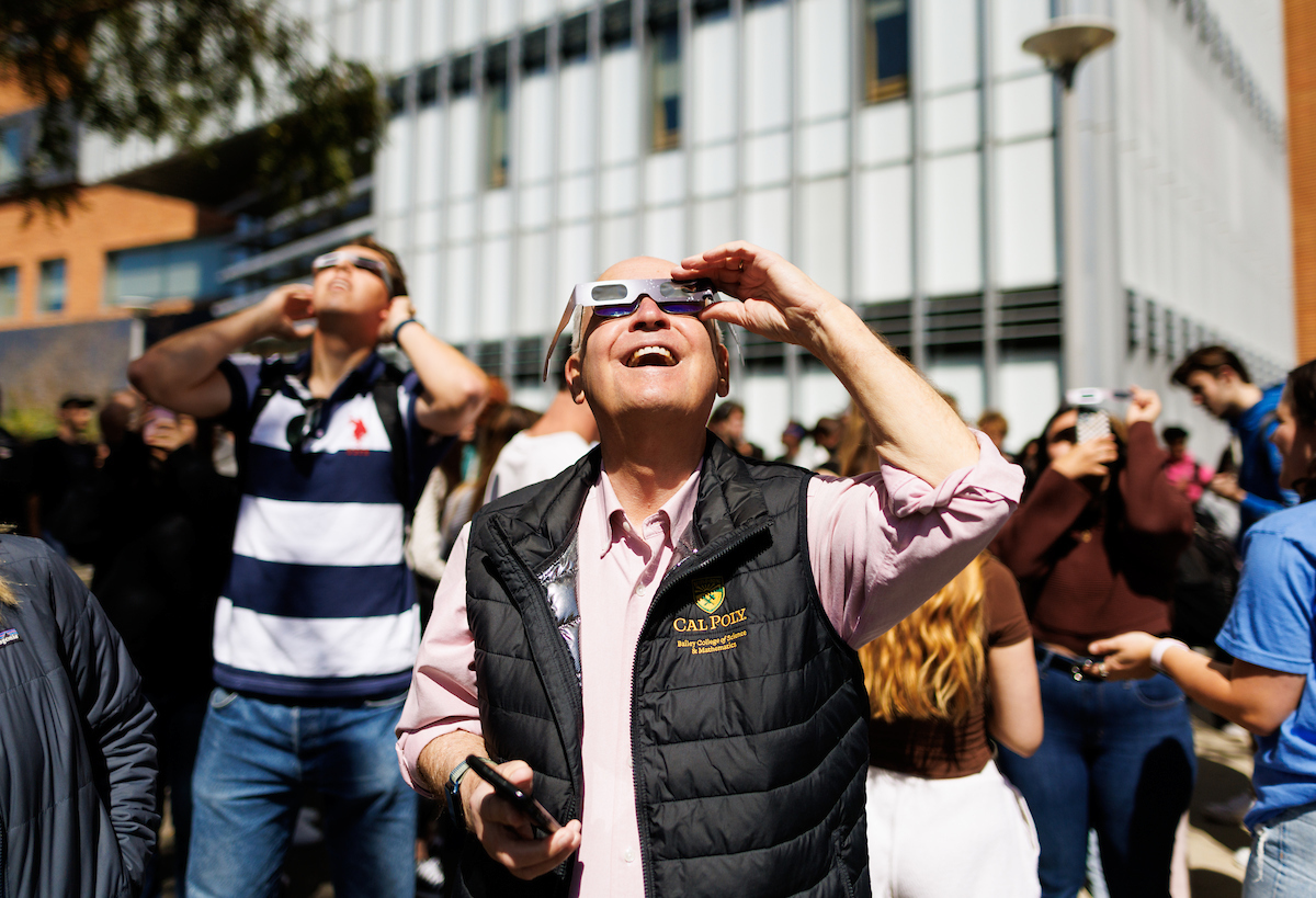 People wearing protective eclipse glasses smile as they look up outside of Baker.