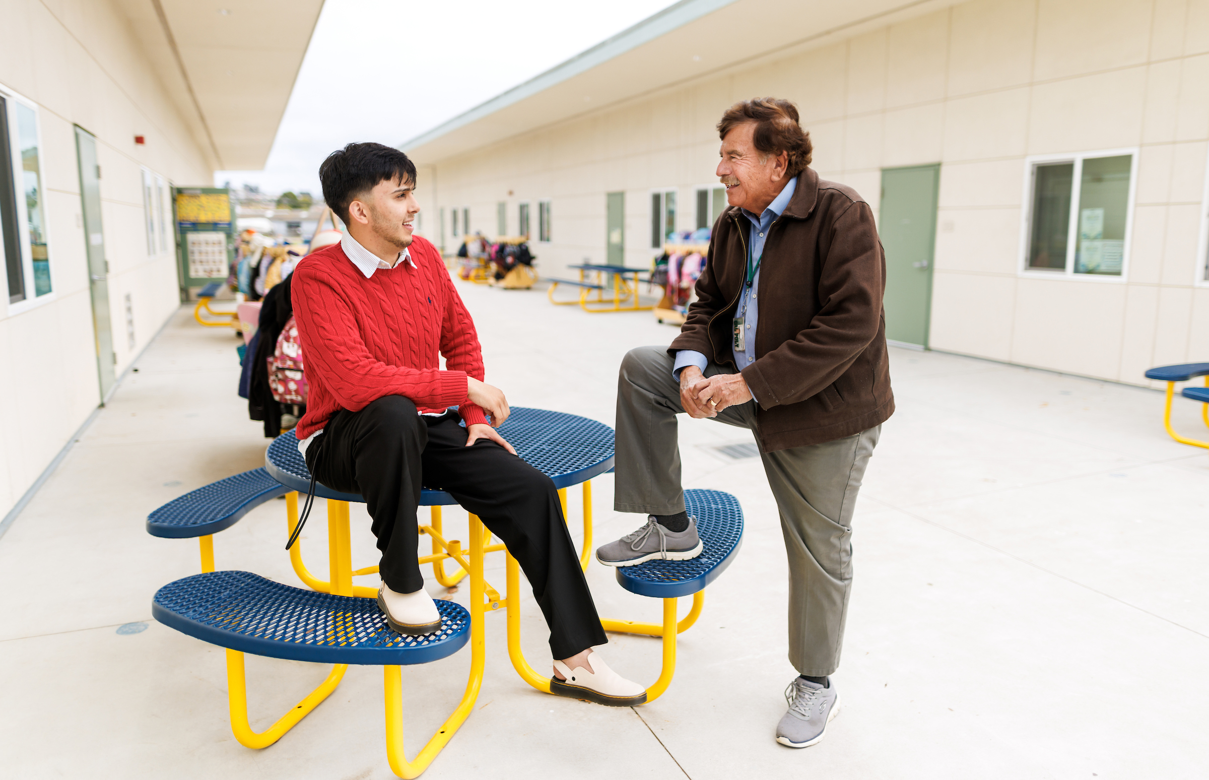 Juan Olivarria and Ramon Gutierrez chat at a lunch table at an elementary school.