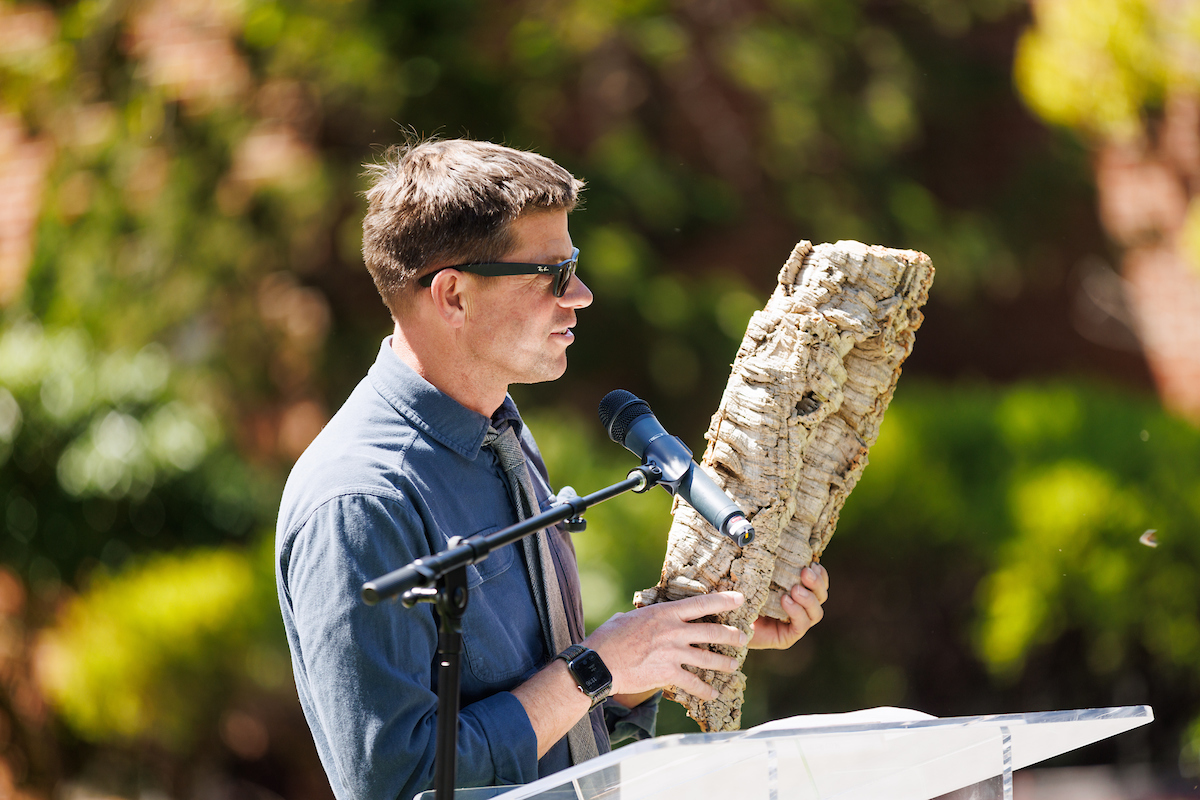 Professor Matt Ritter holds a piece of tree bark and speaks at a podium.
