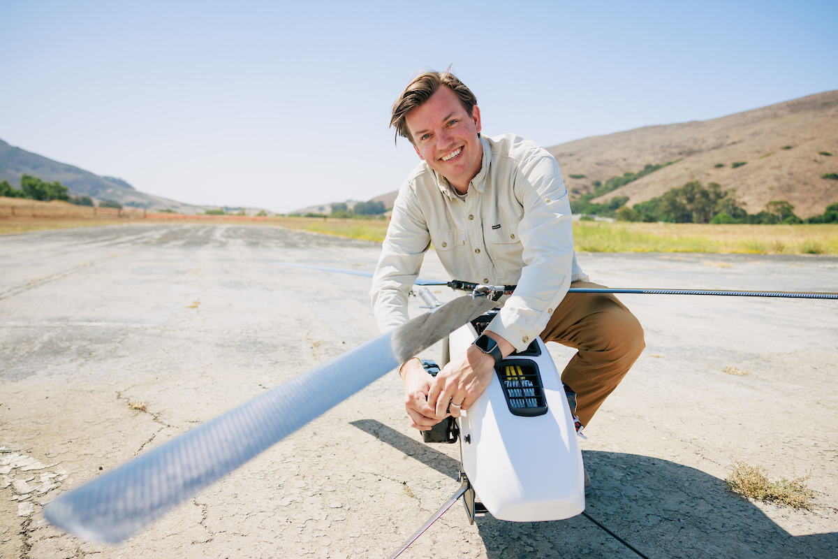 A student kneels on concrete to adjust a white drone.