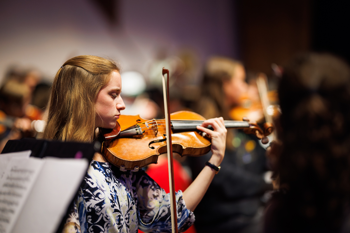 A student plays a violin in an orchestra.