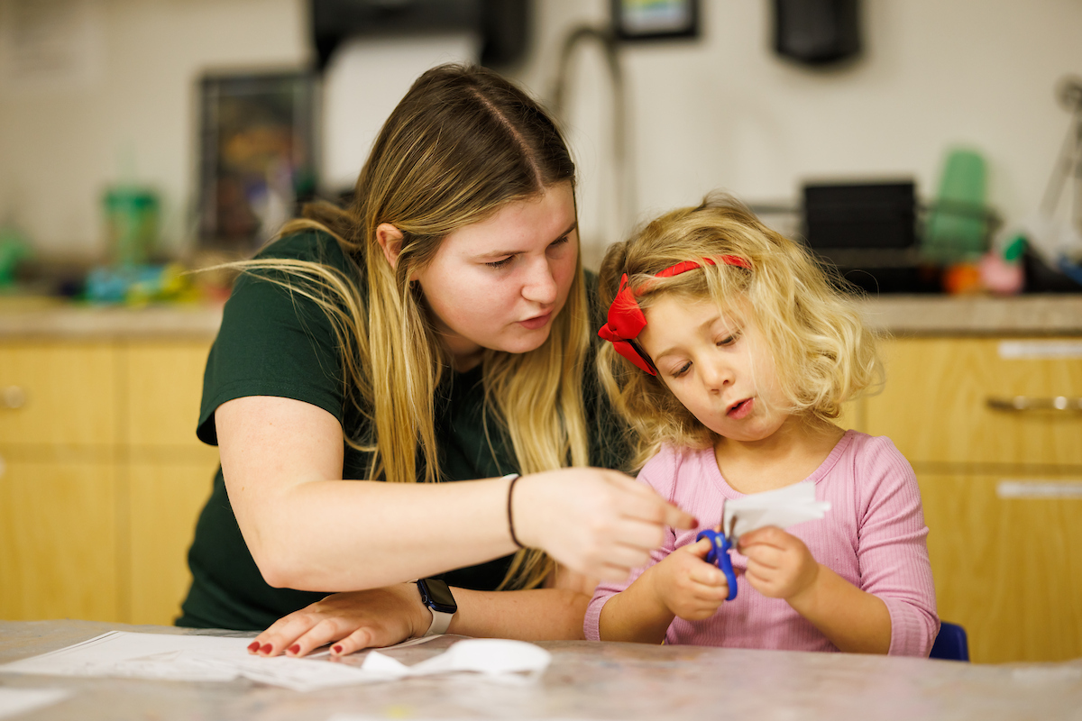 A student and child work together to cut out a paper snowflake at the ASI Children's Center.