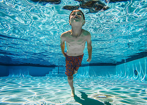 a young boy holds his breath under water in a large swimming pool