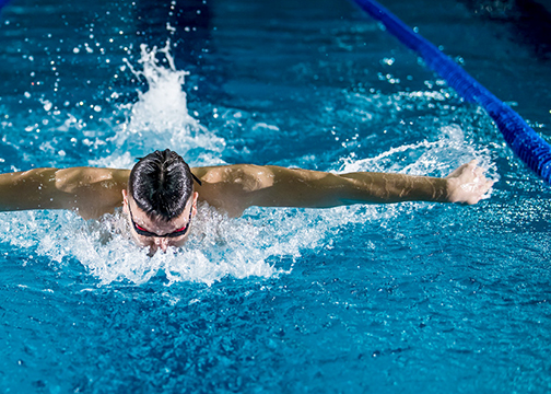 A person swims butterfly at an evening masters lap swim