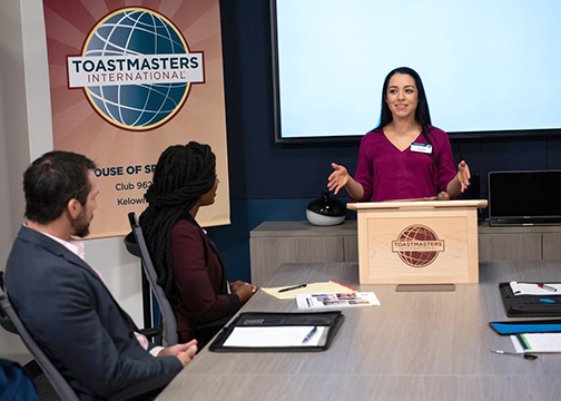 A woman speaks at a Toastmasters podium while two people listen