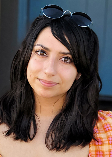 A vertical portrait of masters student Mya Hurtado with sunglasses atop her forehead