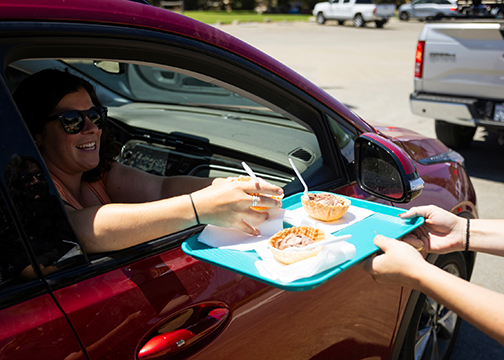 A person smiles in their car as they accept a tray of ice cream scoops from a student worker at the Creamery