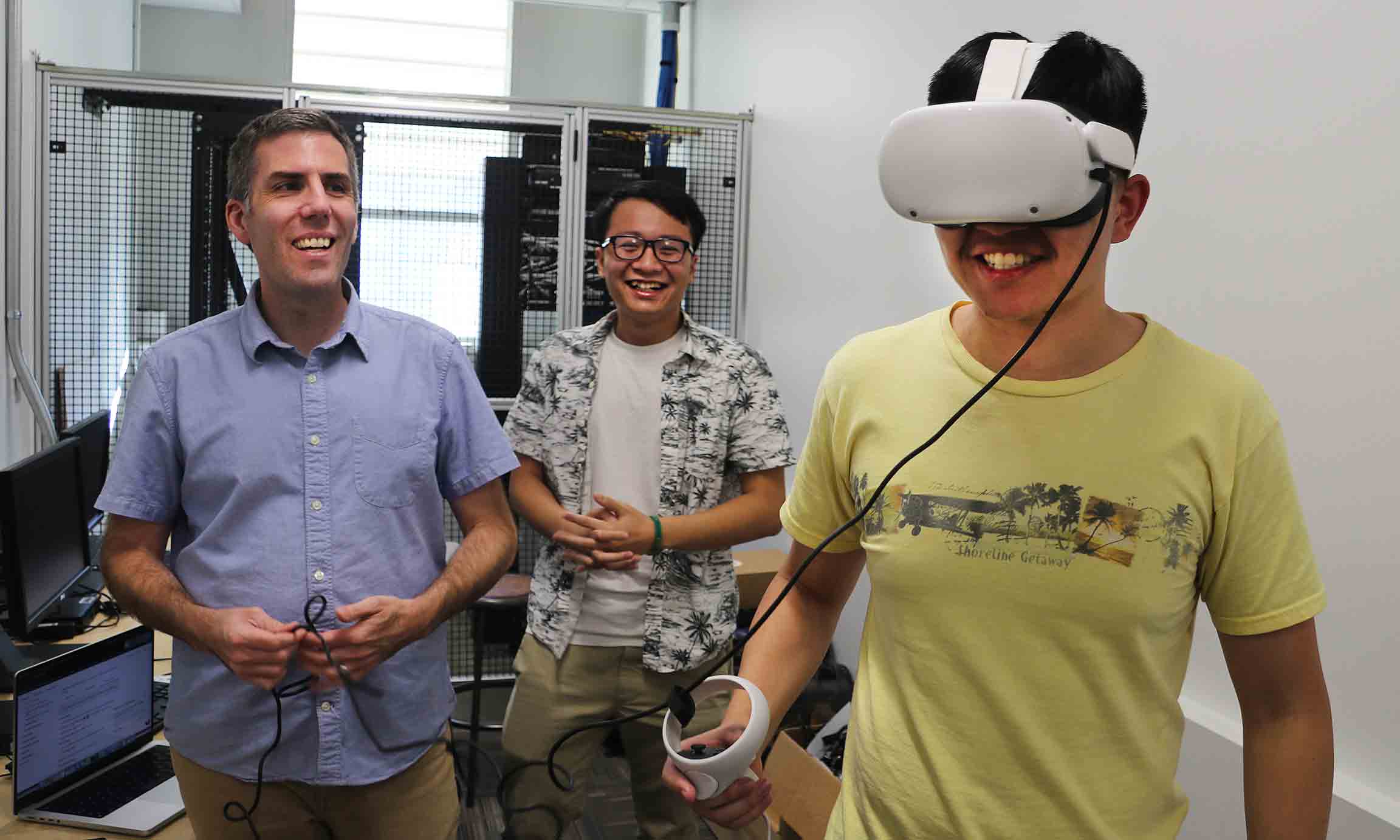 A professor and a student look on as another student wears a VR headset.