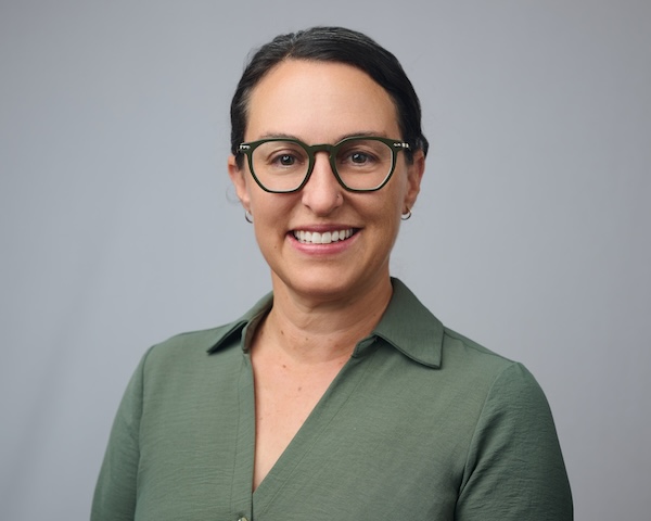 A portrait of Kim Bisheff wearing glasses and a green shirt.