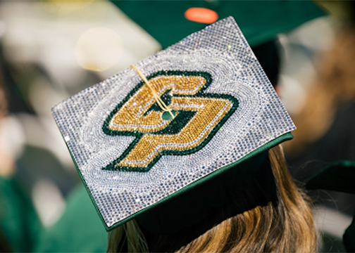 A graduate wears a mortarboard decorated with the Cal Poly logo featuring letters C and P