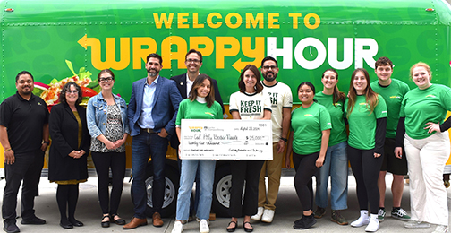 A group of 13 people stand by a Subway banner with two holding a large-size $25,000 check