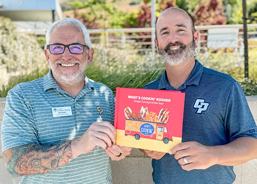 Two Campus Dining officials hold a book titled Whats Cooking Kosher