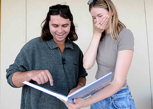A male and female fifth-year architecture students share a smile while looking at the yearbook created to chronicle their timne at cal poly