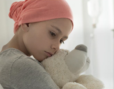 A young girl wearing a head scarf cuddles a bear and looks melancholy