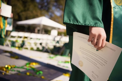 Person in a graduation gown holding a diploma at their side.