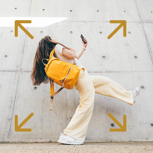 Student in front of a concrete wall kicks leg up in the air.