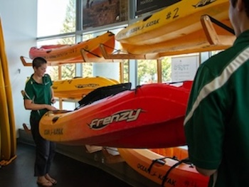 Stacked kayaks and students renting equipment.