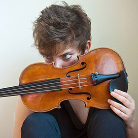 Portrait of Sarah Saviet with a violin in front of the lower portion of her face. 