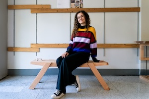 Student sits on wooden bench she designed.