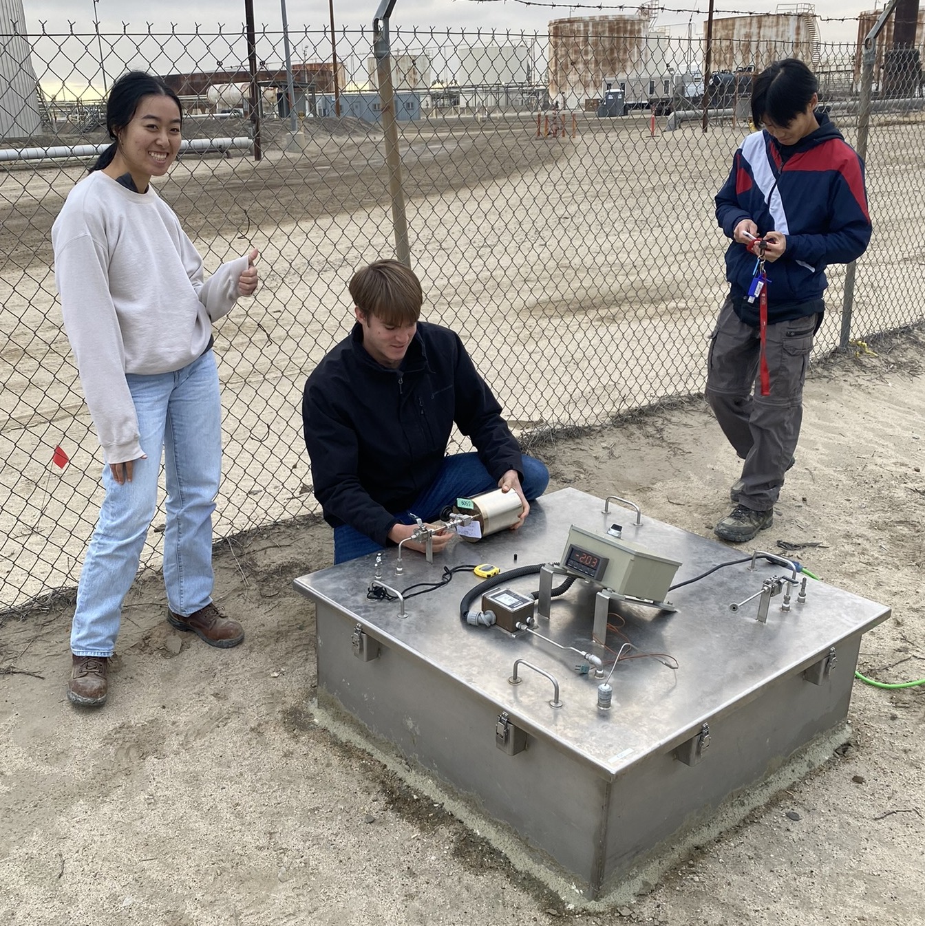 Three students run tests next to a steel box in the ground. 