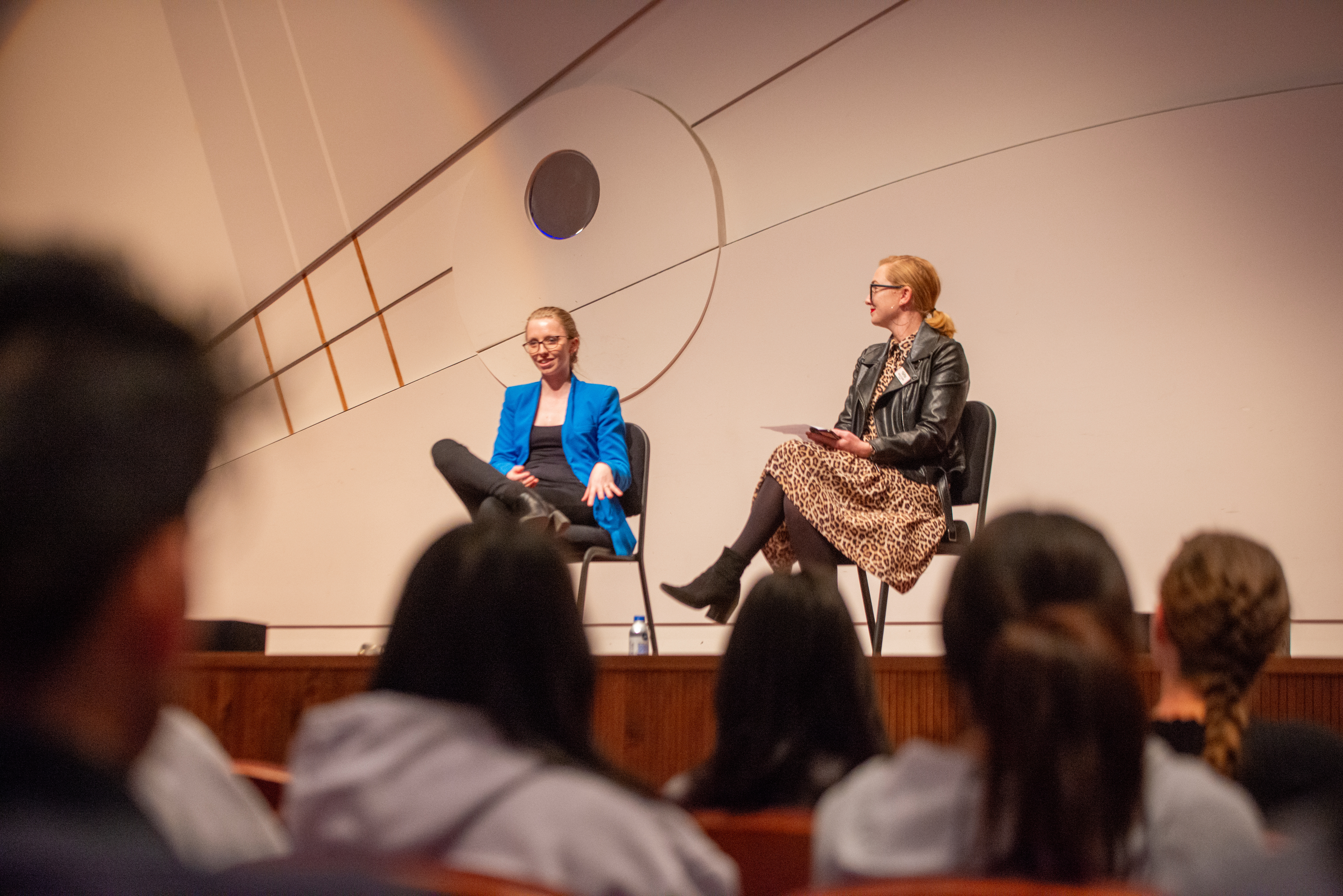 Anna Lapwood, left, and Molly Clark, right, sit on chairs onstage as students sit in the audience.