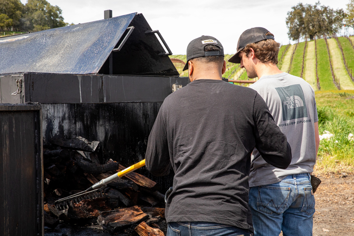 Students rake matter in a biochar kiln outside.