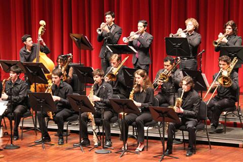 14 student jazz players perform on a stage in front of a red velvet curtain