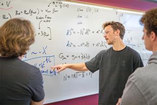 Two students and a professor gather around a whiteboard which contains complicated mathematical equations.