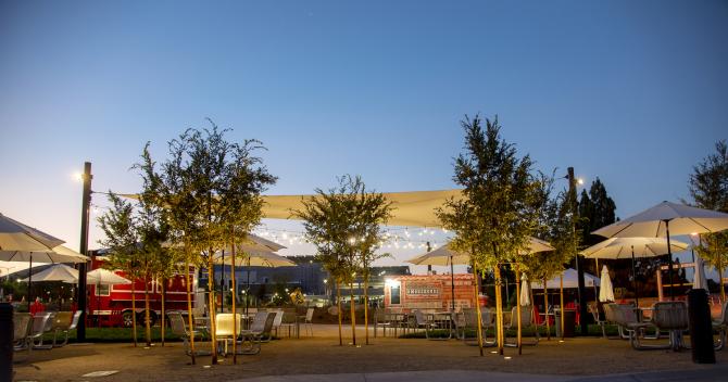 One of Cal Poly's community outdoor spaces, shows food trucks and a warmly lit outdoor dining space at twilight. 