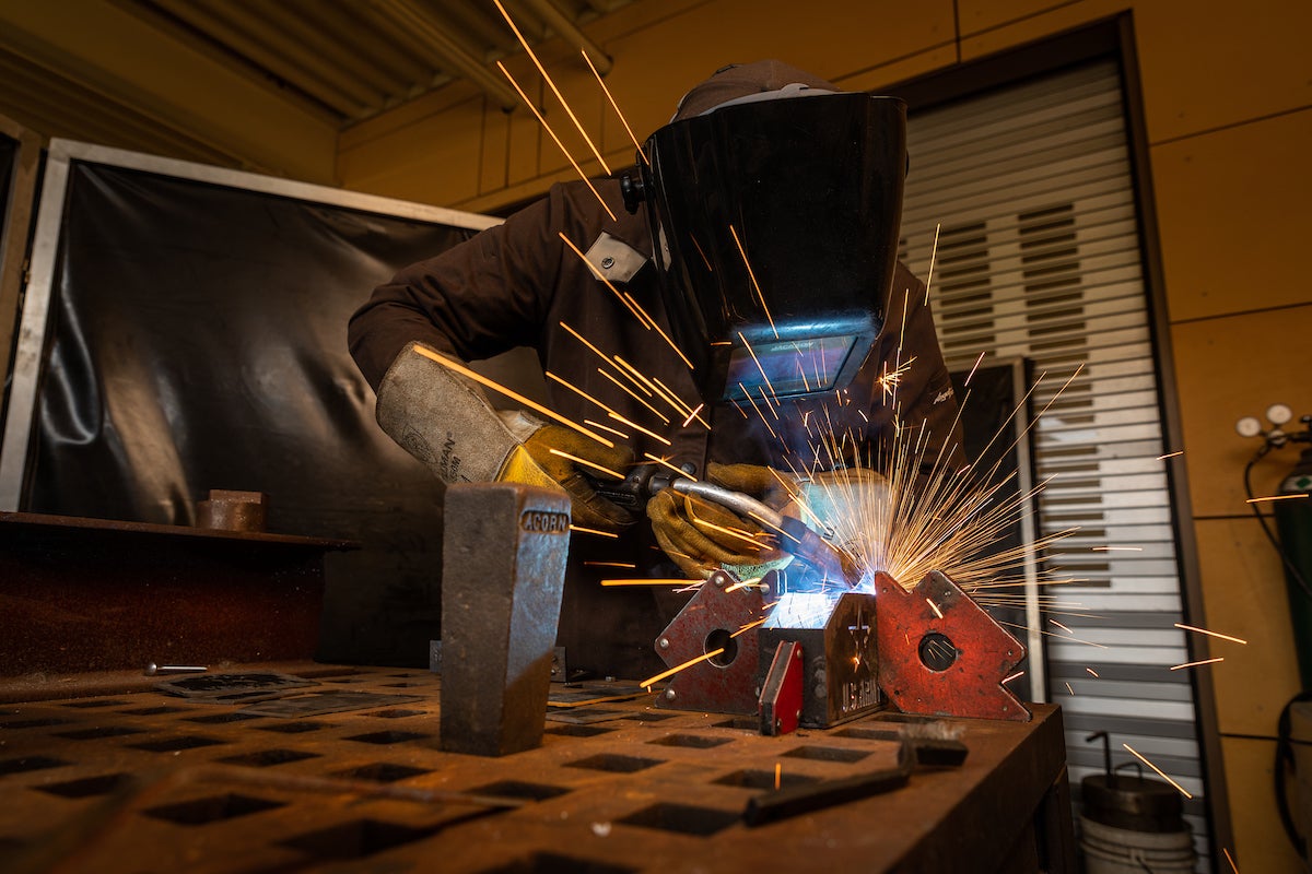 A student wears protective gear as they weld equipment together for their mechanical engineering project.