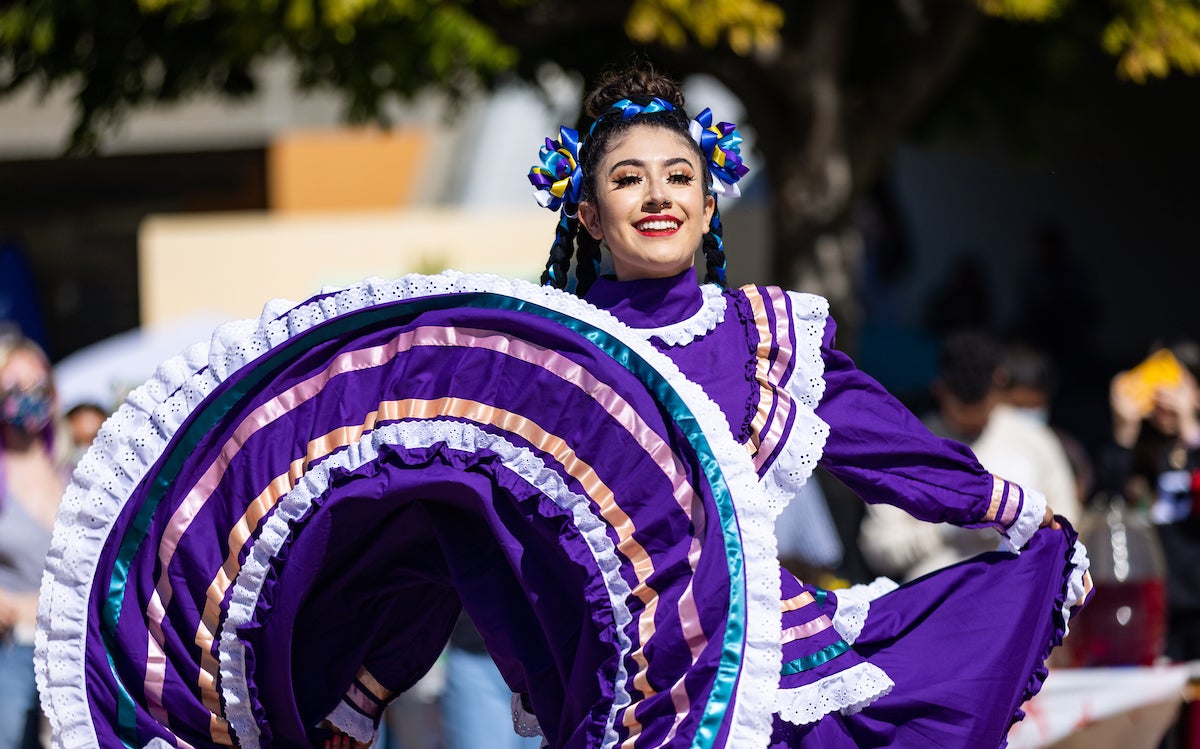 A female student wearing a traditional Mexican foklorico dress smiles as she dances.