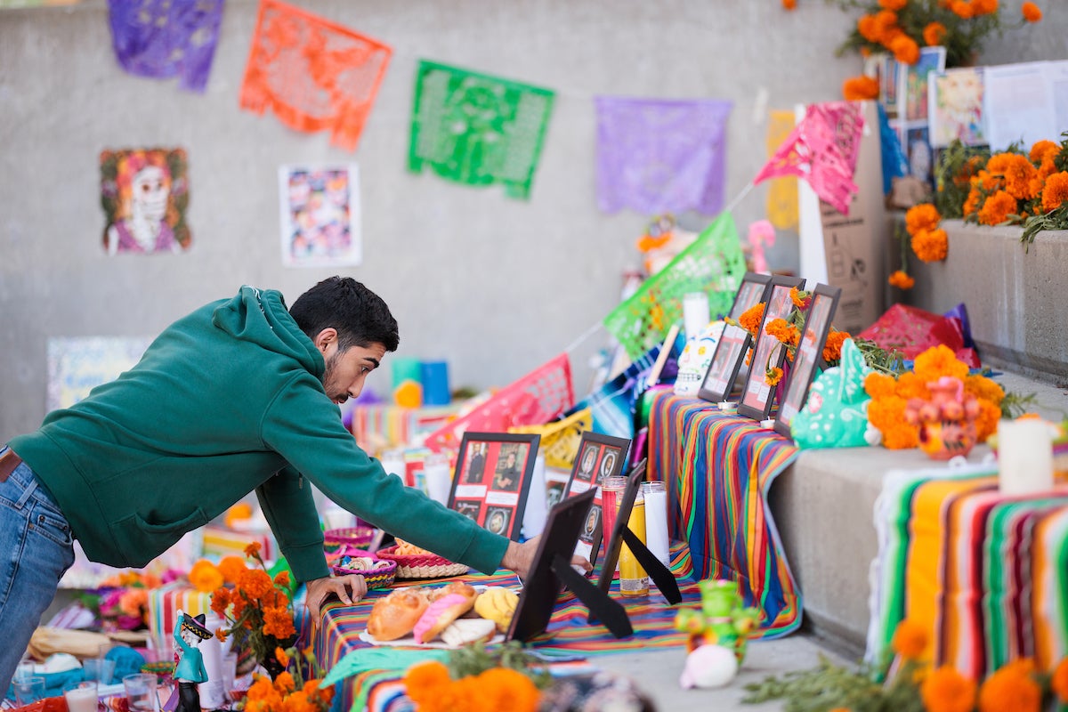 A man wearing a green sweatshirt touches a Dia de los Muertos altar at Cal Poly.