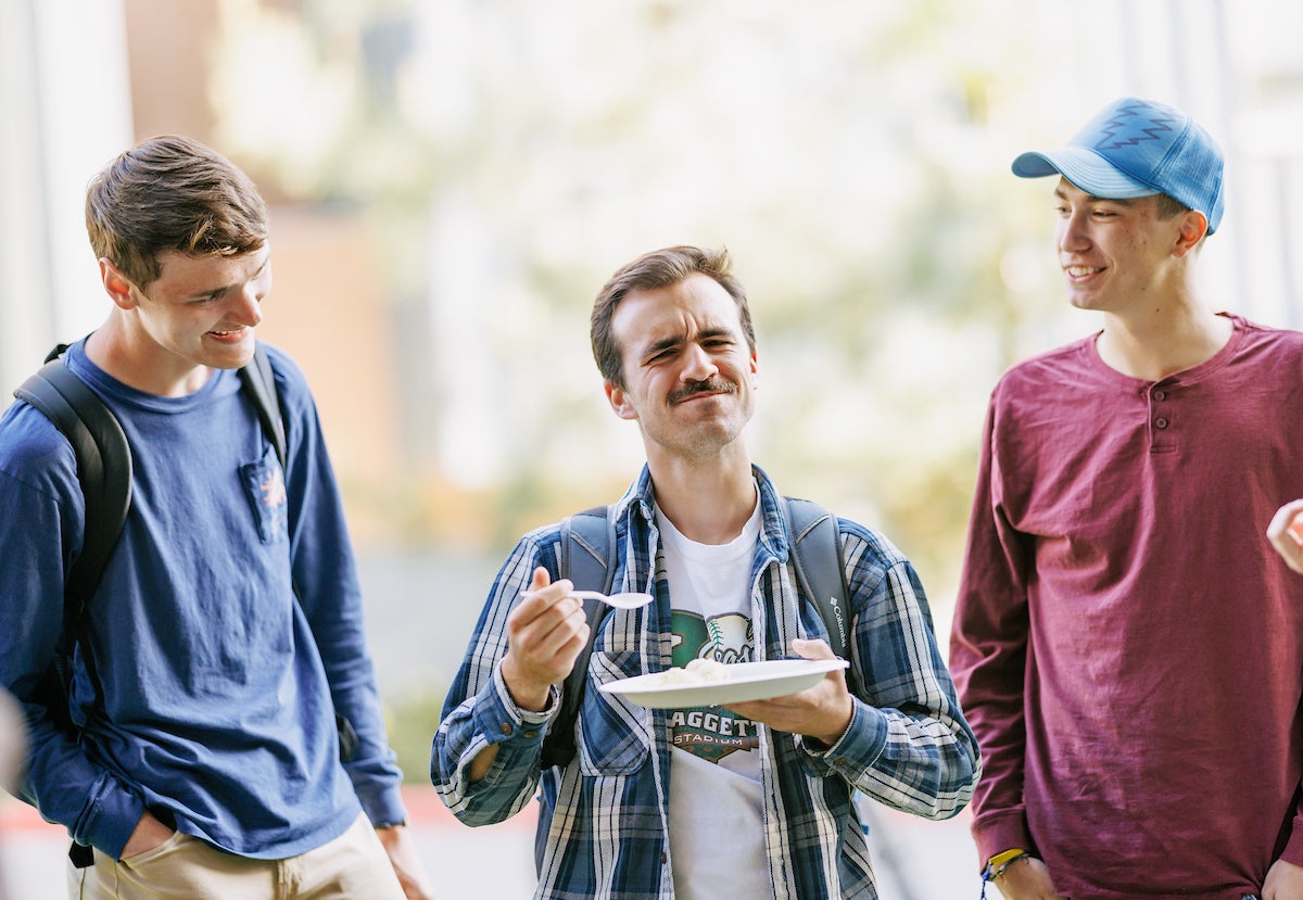 A male student holds a paper plate of durian fruit and grimaces as he tries it.