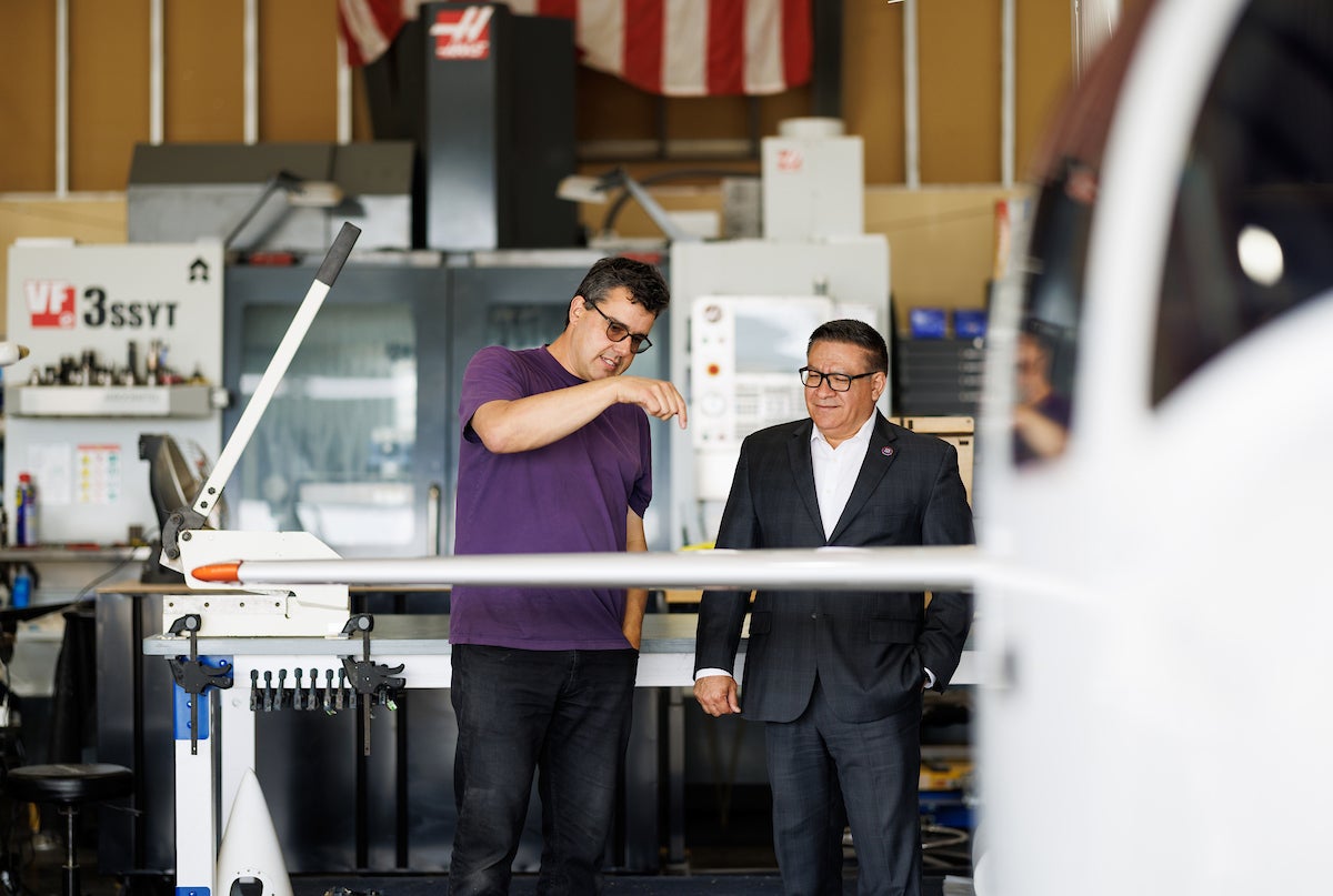 A professor in a purple shirt talks to Congressman Salud Carbajal as viewed from the other side of a small plane.