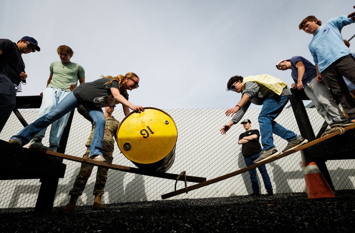 Students push a barrel at another group of students during a ropes course.