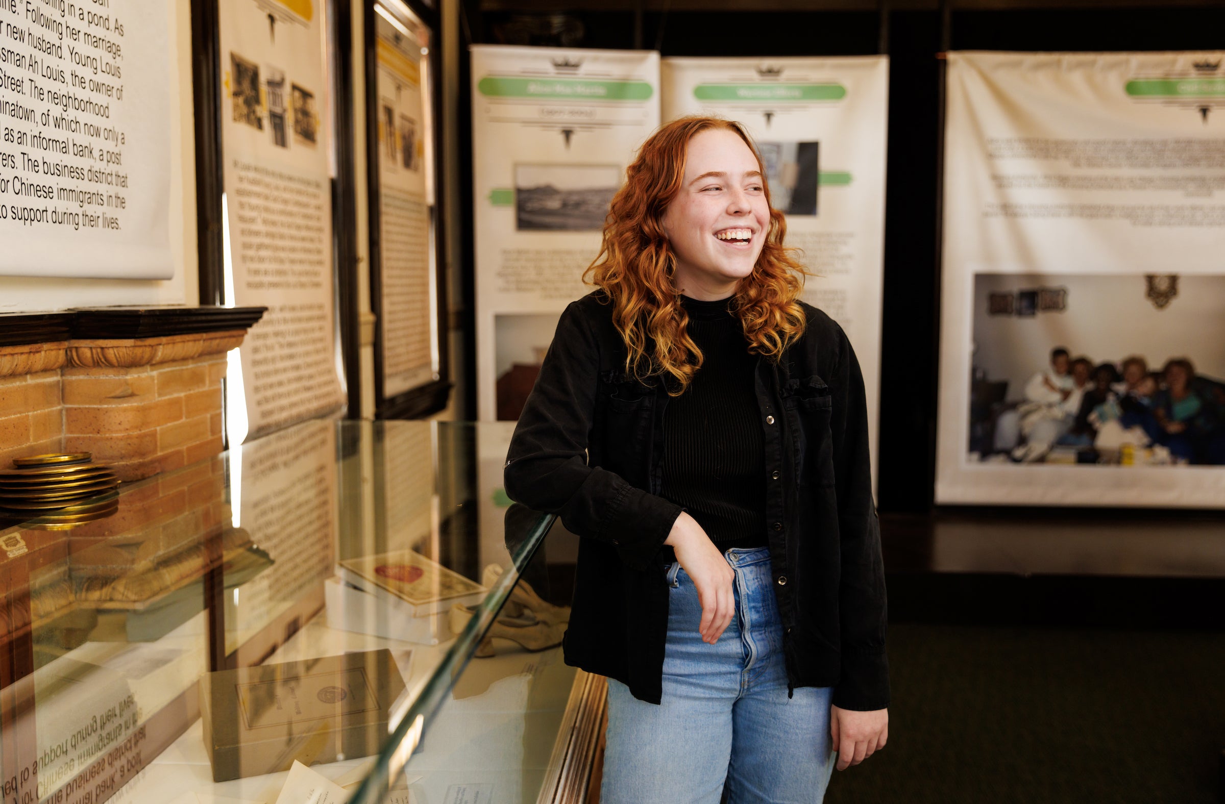 A student leans on a glass case surrounded by posters and memorabilia from the Hidden Voices exhibit.