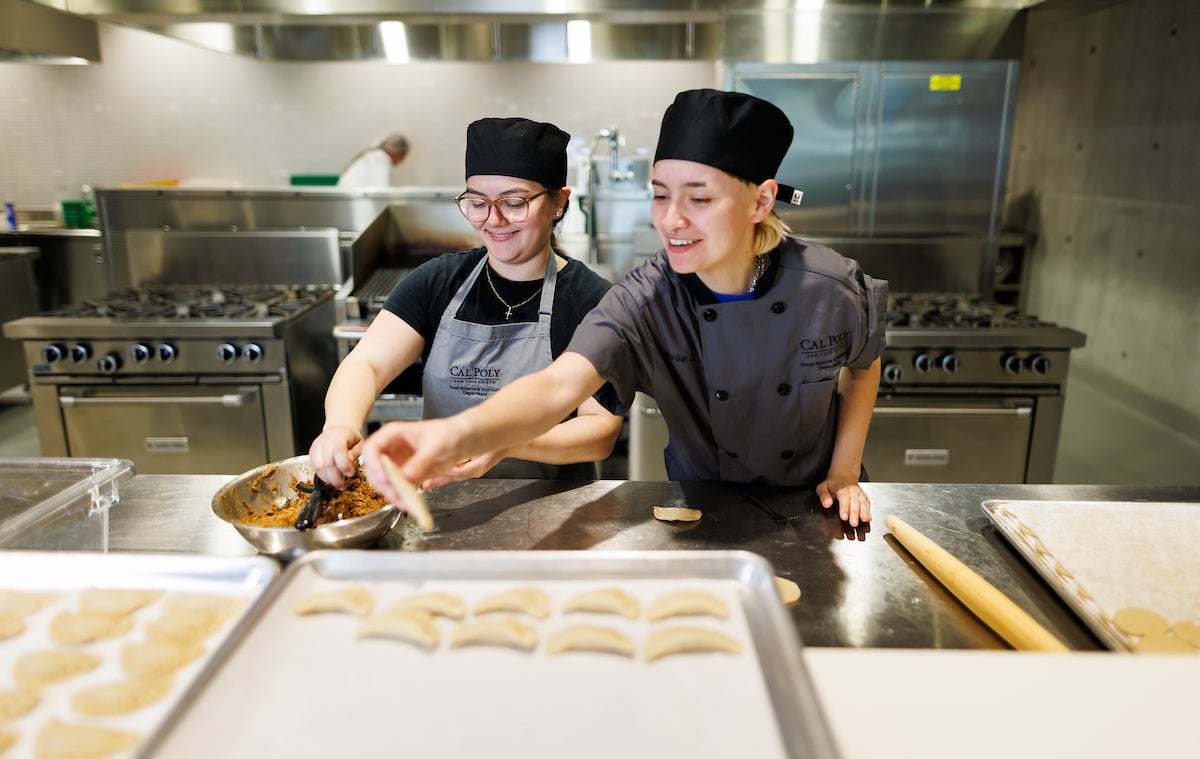 Two students assemble hand pies in a culinary lab.