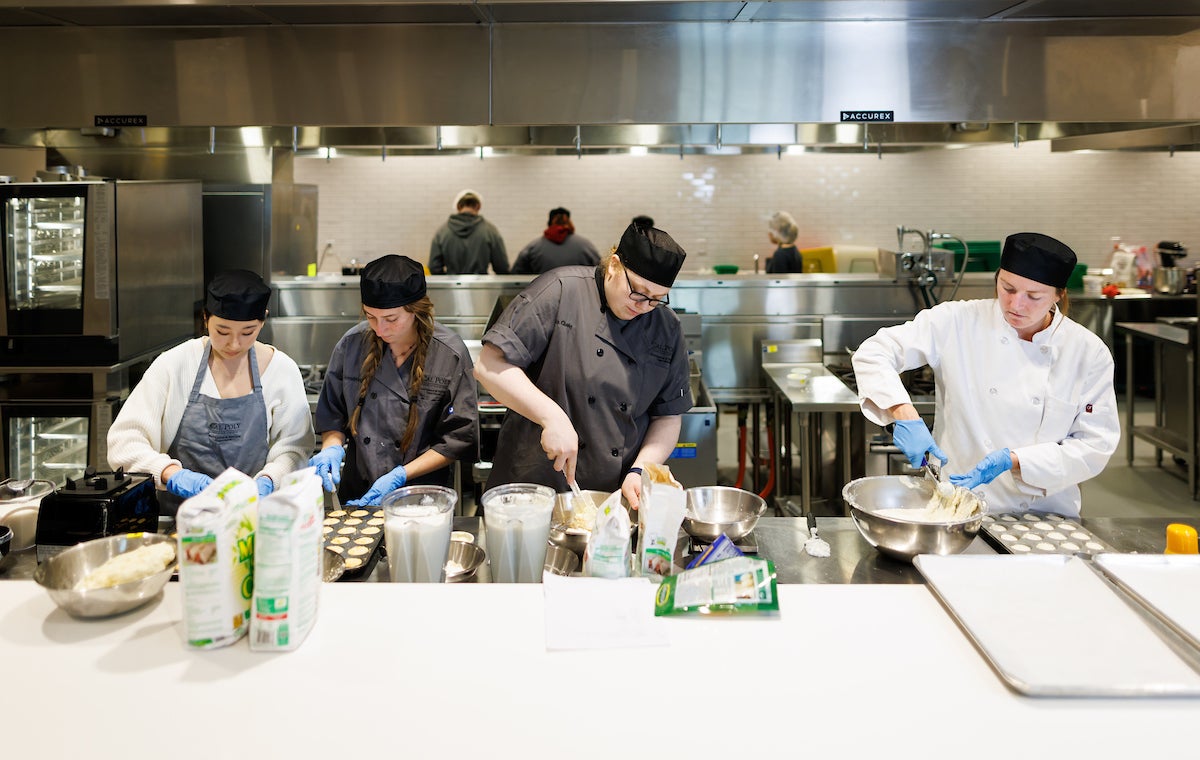 Students in a culinary lab mix batter and prepare food for serving.