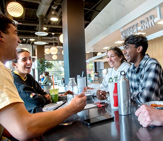 Four smiling Cal Poly students have a meal at Vista Grande