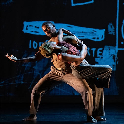 Two dancers, a man and woman are intertwined, the man with an arm extended is dipping the woman as they look at each other