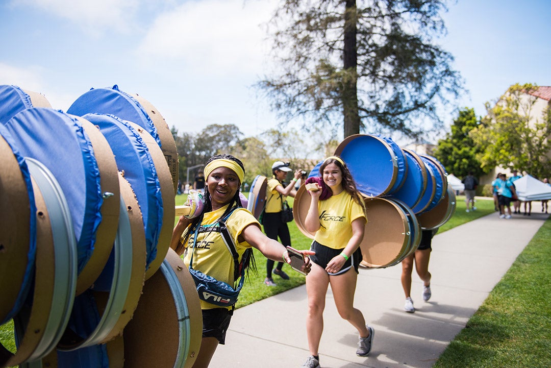 Two young women help carry large round structures up a walkway as part of the Design Village Competition